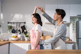 Asian attractive loving couple enjoy dance together in kitchen at home. Beautiful romantic new marriage man and woman wear aporn feeling happy and enjoy activity relationship in house listen to music.