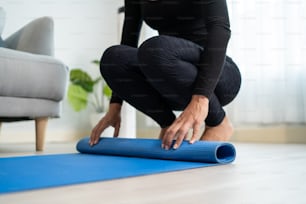 Close up short of young sportswoman hand roll out exercise mat at home. Beautiful active skinny sport girl prepare to start work out by doing yoga stretching body for health in living room in house.