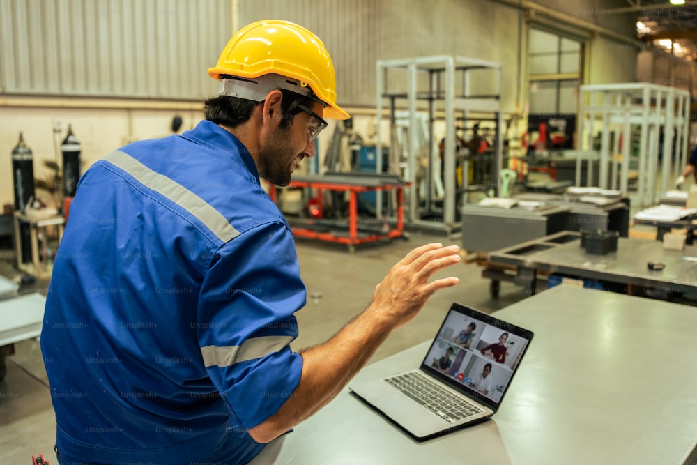 Caucasian handsome male industrial worker work in manufacturing plant. Attractive young man industry factory engineer use laptop computer video call with team to processes product manufacturing plant.