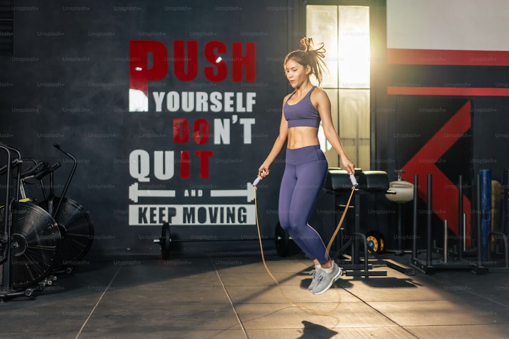 Asian athlete woman workout to maintain muscle in fitness gym club. Attractive young sportsfemale exercising by using jumping rope to burns calories and strengthens body for health care in stadium.