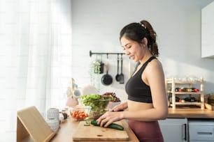 Asaian attractive woman wear sport clothes cook green salad in kitchen. Young beautiful girl feeling happy and enjoy eating vegetables healthy foods to diet and lose weight for health care in house.