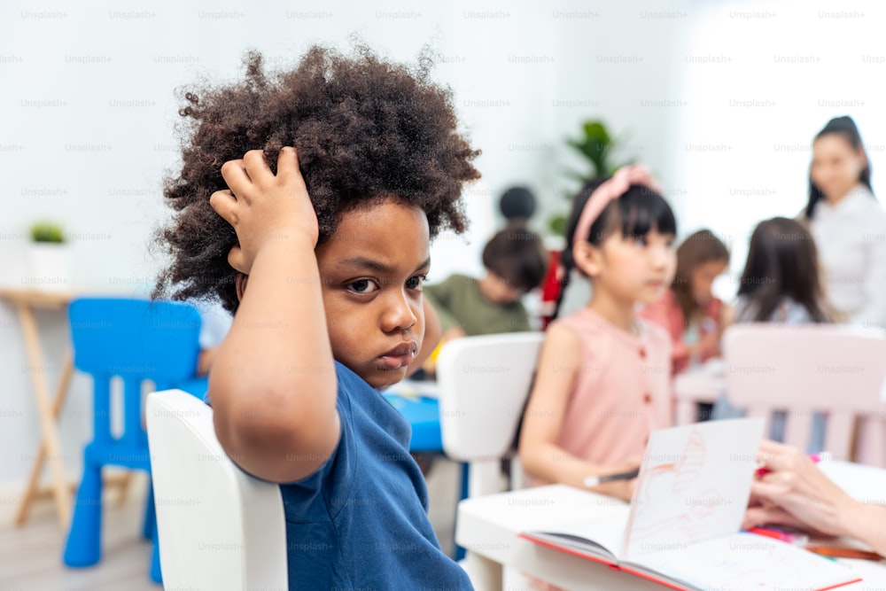 Portrait of Stressed African black child boy sitting in classroom. Depressed student little kid young boy feeling tired and worry while study art and drawing in schoolroom and look at camera at school