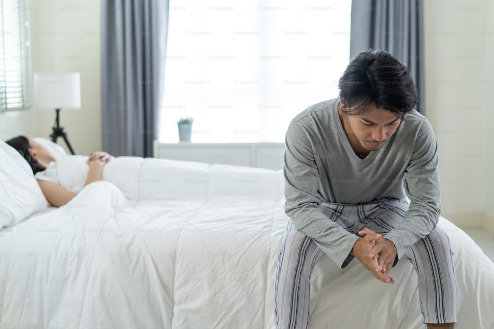 Asian young man feel angry girlfriend having conflict domestic problem. New marriage man and woman feel heartbroken for quarrel conflict while sit on bed in bedroom. Family problem-separation concept.