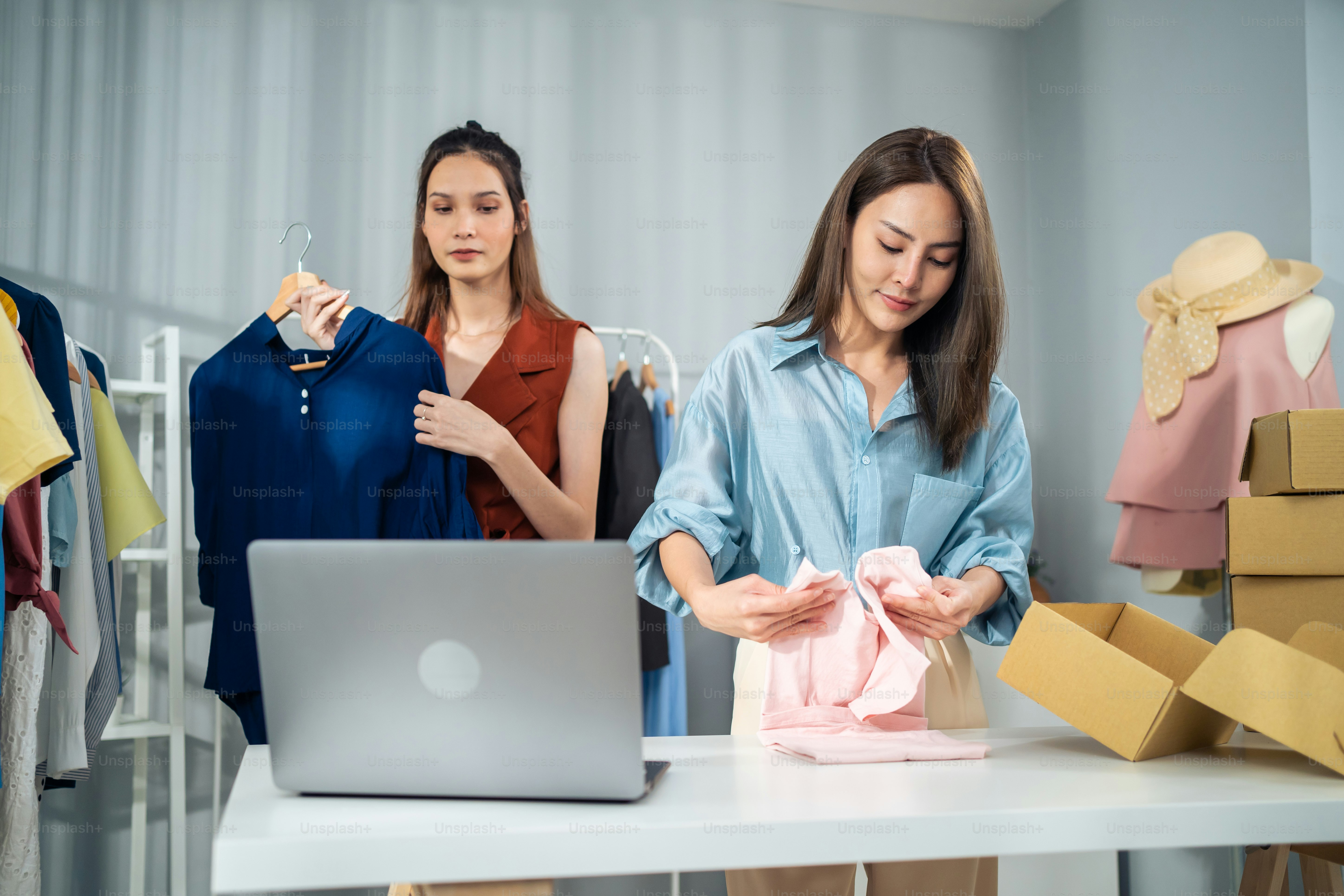 Asian woman friends couple packing clothes order into box for customer. Young attractive business people work to preparing parcel boxes check ecommerce shipping online retail to sell at office store.