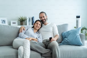 Caucasian loving couple watch movie together in living room at home. Beautiful happy new marriage man and woman sit on sofa use remote control TV show and have fun laughing look to television in house