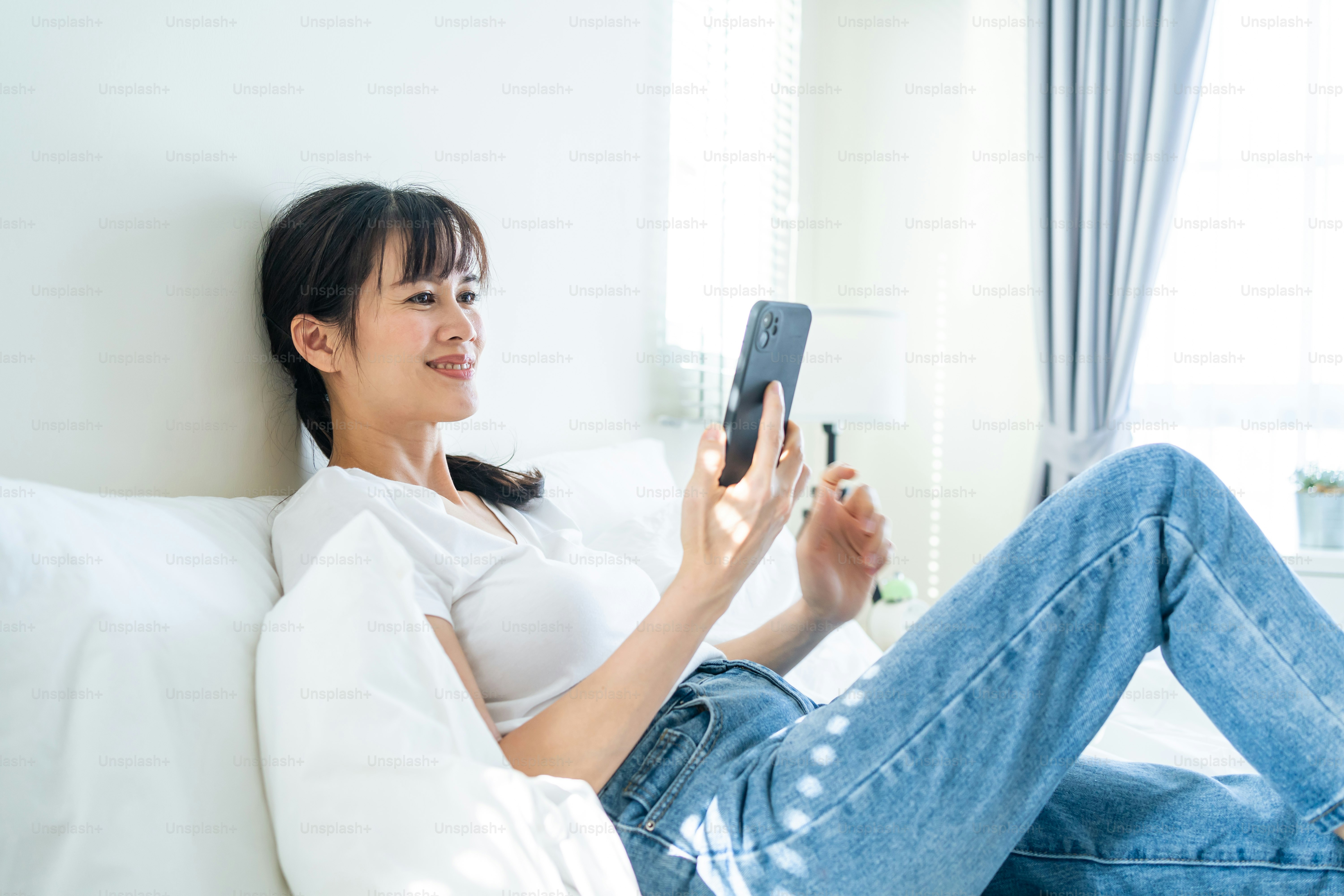 Asian attractive woman use mobile phone chat on bed at home in morning ...