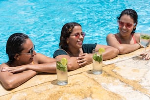 Young girls having a party with cocktails in a pool, toasting with cocktails and smiling. Shot on a sunny summer day.