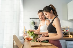 Asian young two women sibling in sportswear cooking salad in kitchen. Active beautiful girl sister feel happy and enjoy eating vegetables healthy foods to diet and lose weight for health care in house