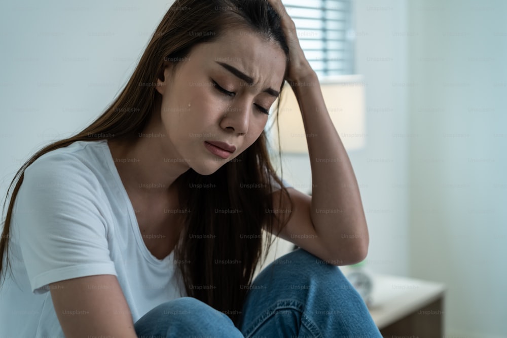 La bella ragazza asiatica della depressione che piange in lacrime si siede sul letto in camera da letto. Attraente giovane donna infelice che si sente triste, sola e sconvolta con il problema della vita e tiene il tessuto sulle mani nella stanza buia della notte a casa