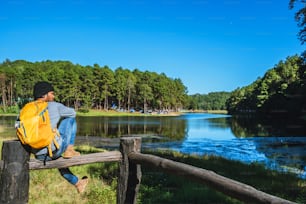 若い男性は、湖や美しい池のある山の自然の中を旅します。湖の視点の上に立っているバックパックを持つ旅行者、休暇中にリラックスする観光。