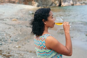 A woman drinking a glass of wine against the backdrop of a sunny view by the sea.