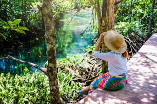 Asian women travel relax, travel nature in the holiday. Nature Study in the forest. women happy enjoying sitting and watching the lake mangrove forest. tha pom-klong-song-nam at krabi. summer