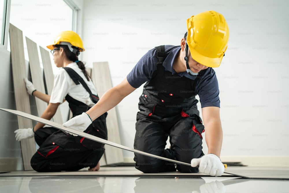 Los trabajadores artesanos asiáticos instalan tableros laminados en el piso de su casa. El atractivo carpintero y carpintero revisa y cuenta el parquet para ayudar al constructor a reparar el pasillo para renovar el apartamento o la casa.