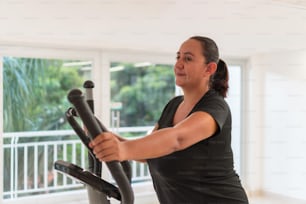 Una mujer que intenta perder peso en casa, hace un entrenamiento elíptico