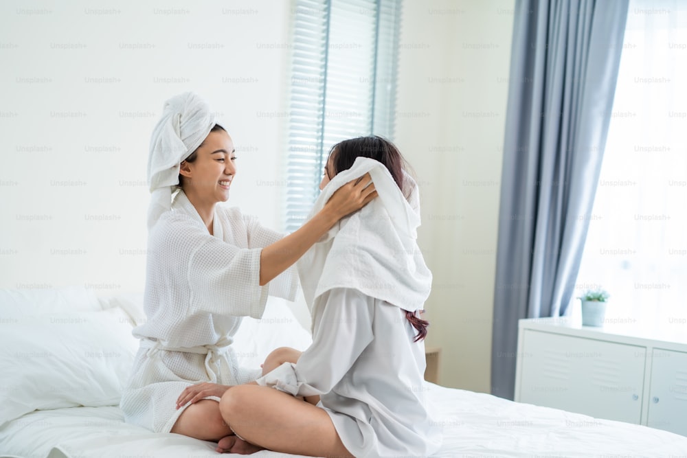 Asiatisches schönes lesbisches Paar verbringt morgens Freizeit zusammen. Attraktives romantisches Mädchen im Schlafanzug, das die Haare der Freundin nach dem Duschen auf dem Bett im Schlafzimmer im Haus trocknet. Homosexuelle-LGBTQ-Konzept.