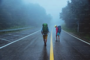 恋人アジア人男性とアジア人女性は自然を旅します。車道を歩きます。自然を楽しく旅する。雨が降る霧の中。梅雨の時期。
