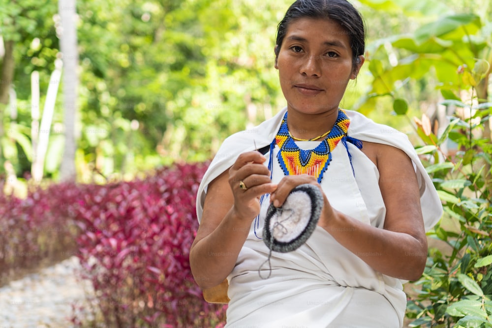 Colombian woman in traditional clothing weaving looking at the camera