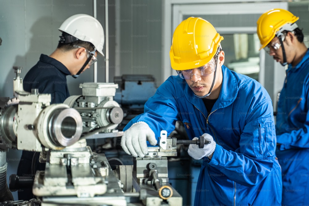 Asian mechanical workers working on milling machine. The technicians wearing protective glasses and helmet when operating the machine for safety precaution. The man working carefully prevent dangerous