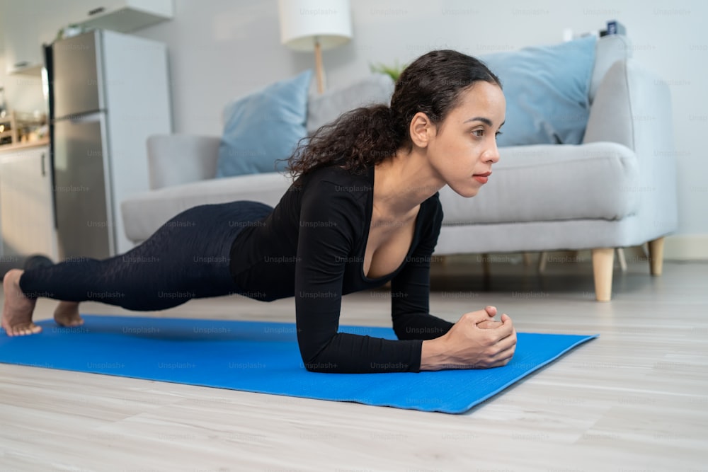 Latino beautiful young woman stay home, doing cardio exercise at home. Active sport girl doing lockdown activity workout plank on floor follow instruction video from online trainer for health in house
