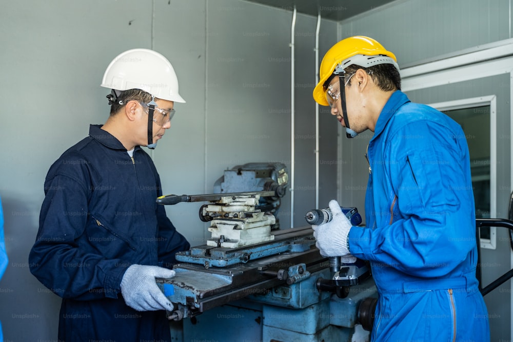Trabajadores mecánicos asiáticos trabajando en una fresadora. Los técnicos usan gafas protectoras y casco cuando operan la máquina por precaución de seguridad. Líder que asesora a un miembro de su equipo que realiza un trabajo