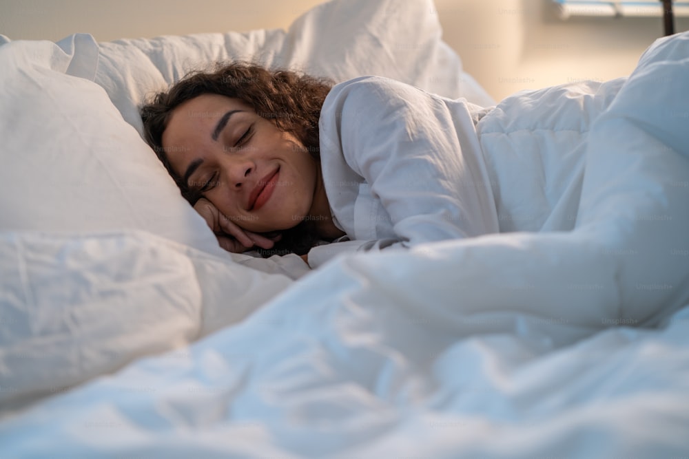 Latino mulher bonita deitada na cama no quarto no quarto escuro da noite. Jovem atraente fêmea de pijama dormindo sozinha no travesseiro confortável e cobertor aconchegante no quarto silencioso para cuidados de saúde em casa.