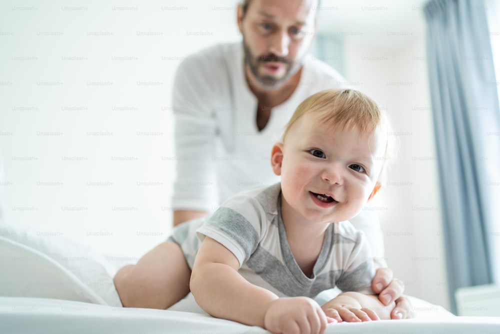 Caucasian parents play with cute baby boy child infant on bed at home. Happy family, attractive handsome dad look to toddler son crawl with happiness enjoy after wake up activity in bedroom in house.v