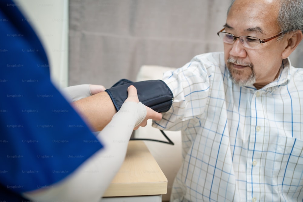 Asian young woman nurse at nursing home taking care of senior elderly man sit on sofa. Caregiver Therapist doctor examining an older patient use blood pressure gauge. Medical insurance service concept