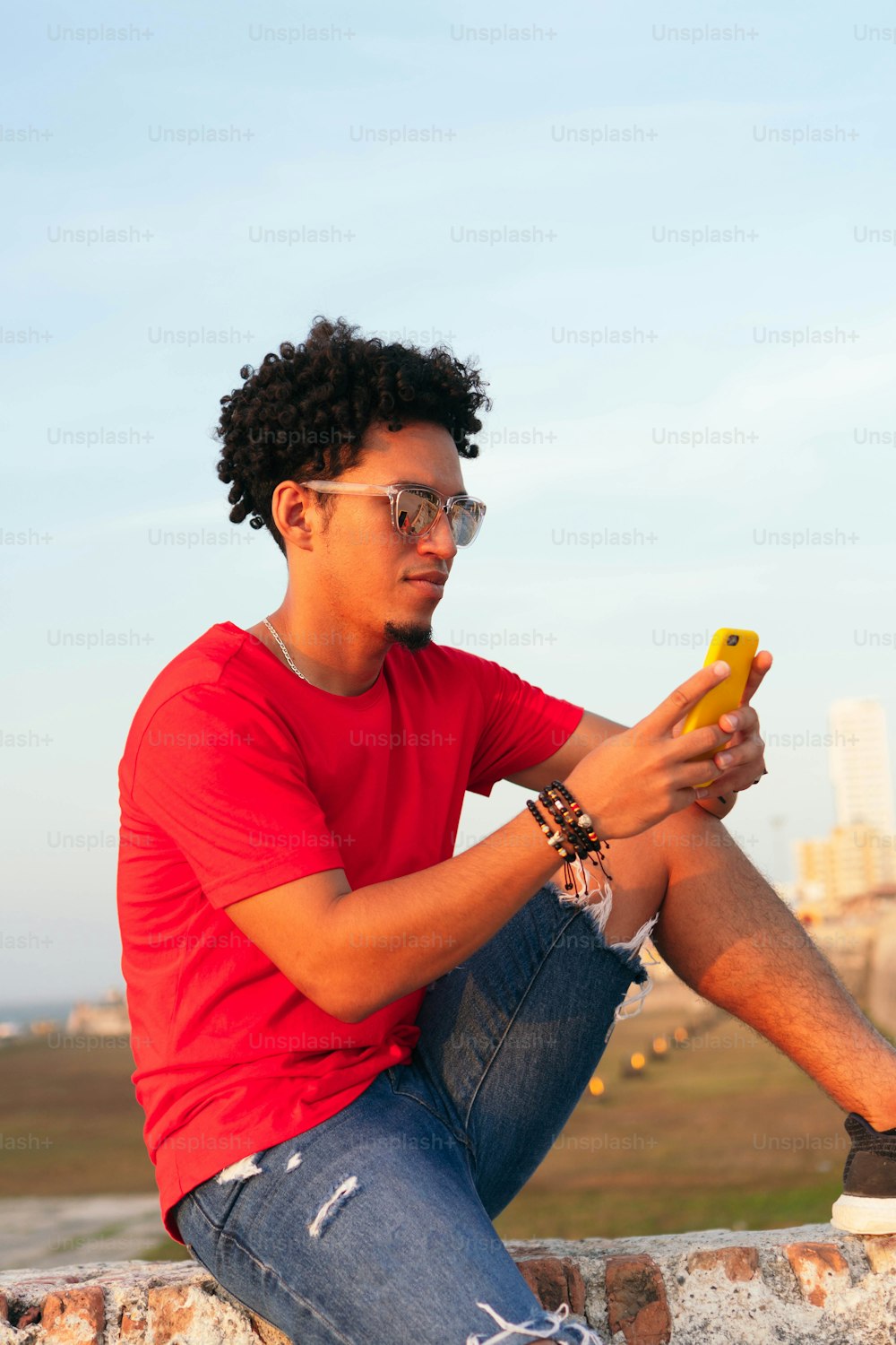 Homem hispânico de cabelos encaracolados verificando seu telefone celular ao ar livre