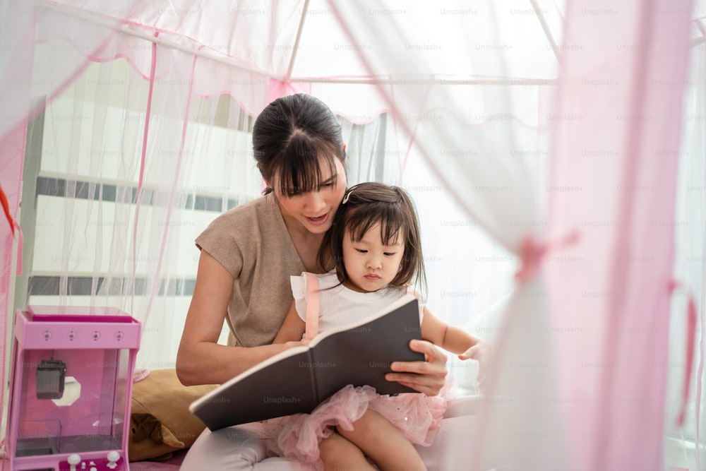 Asiatische schöne liebevolle Mutter las Geschichtengeschichte für junge kleine Mädchen Tochter im Zelt zu Hause. Eltern spielen Bildungsspiel Bilderbuch mit Kind, um Lernfähigkeit zu entwickeln. Erziehungsaktivität im Hauskonzept