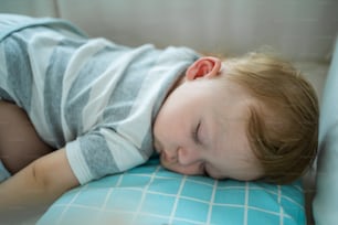 Caucasian baby boy toddler sleep on kids bed with comforter in bedroom. Adorable newborn infant having sweet dream, lying down on cozy pillow and warm blanket alone in house. Child-development concept