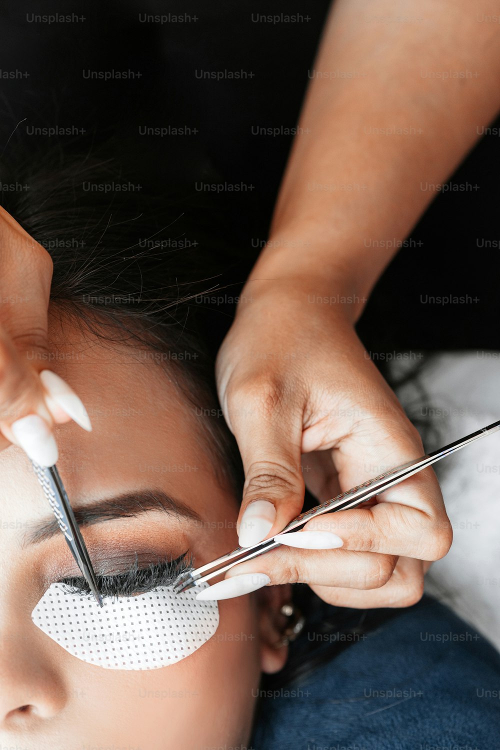 Hands holding tweezers while performing eyelash extension attachment.