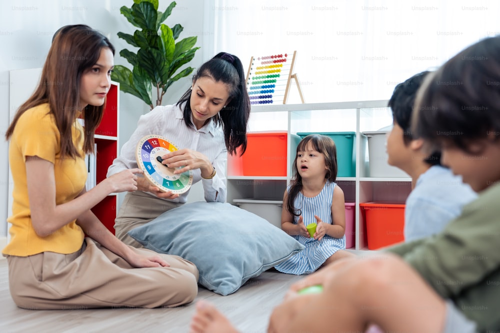 Caucasian beautiful young woman teacher teaching art to kids at school. Attractive Instructor master female explain and educate drawing and painting with student kindergarten pre school in classroom.