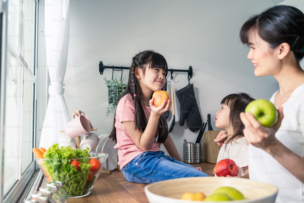 Asian happy family, mother spend time with young daughter in kitchen. Loving beautiful parent mom and little sibling cute girl child feel happy enjoy eat apple for health at home. Healthy food concept