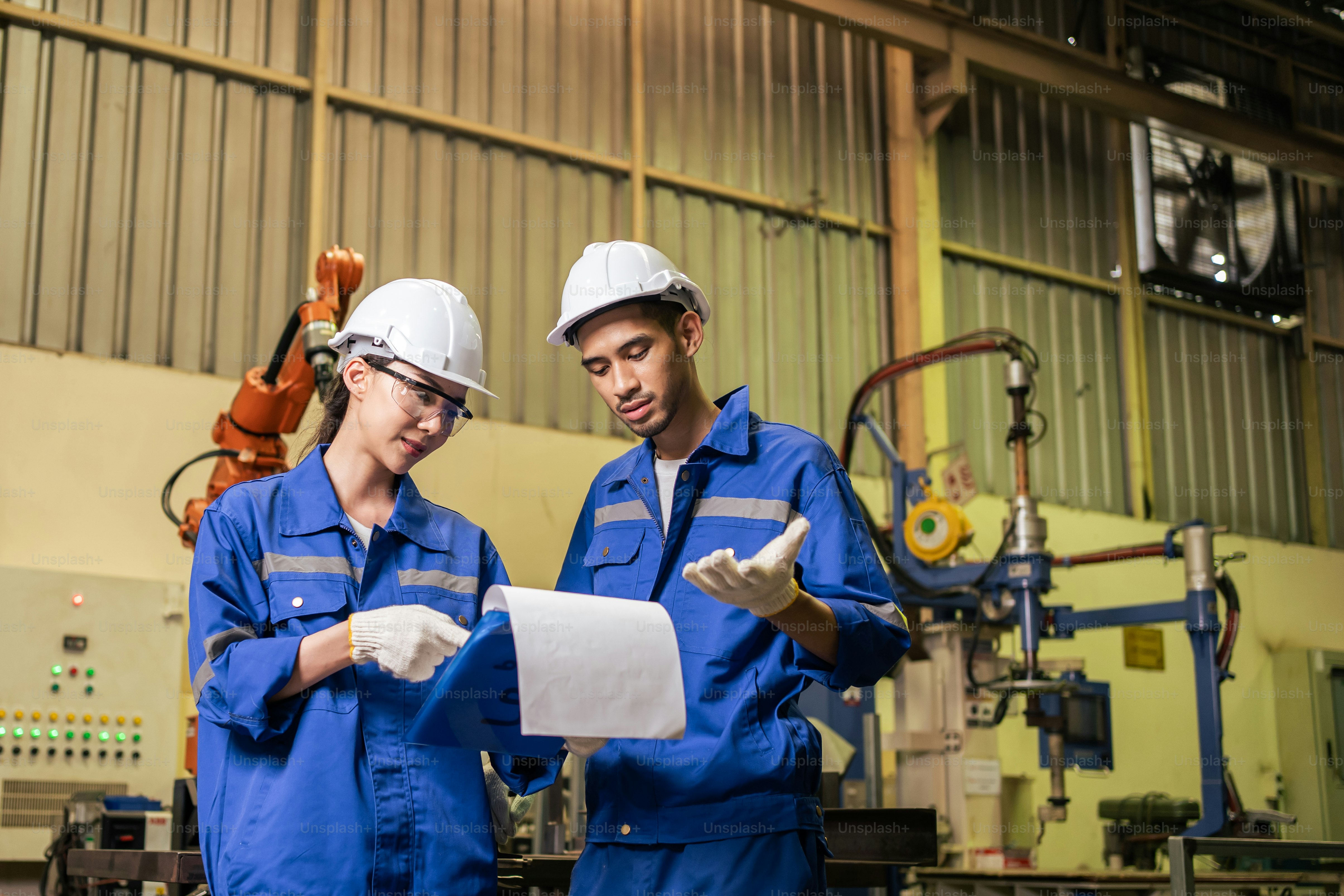 Asiatische Industriearbeiter und -frauen, die in Produktionsbetrieben arbeiten. Attraktive Industrie-Fabrikingenieure tragen Helm und bearbeiten Aufträge und Produkte im Manufakturlager mit Freude