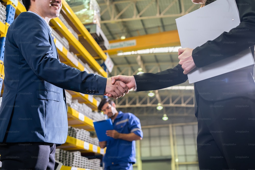 Asian businessman and woman handshake after negotiation in manufactory. Attractive industry factory engineer people talking about business deal, merger and acquisition at manufacturing plant warehouse