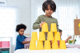 Asian two little friends kid boy playing toy together in schoolroom. Two child student enjoy, spending time play toy stacks cup while during break with feeling fun together in classroom at school.