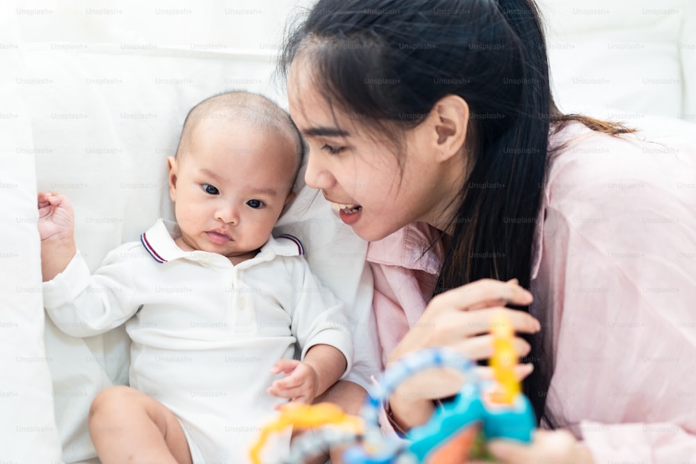 Bebé lindo asiático y madre joven jugando al juguete en la cama en casa. El bebé sonríe y mira el juguete sintiéndose disfrutado y feliz con mamá. Juguete infantil para la educación. Concepto de desarrollo de habilidades para padres y bebés.