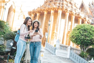 Amiche asiatiche turiste che usano lo smartphone e godono di visite turistiche durante il viaggio nel tempio del buddha di smeraldo, Wat Phra Kaew, popolare luogo turistico a Bangkok, Thailandia