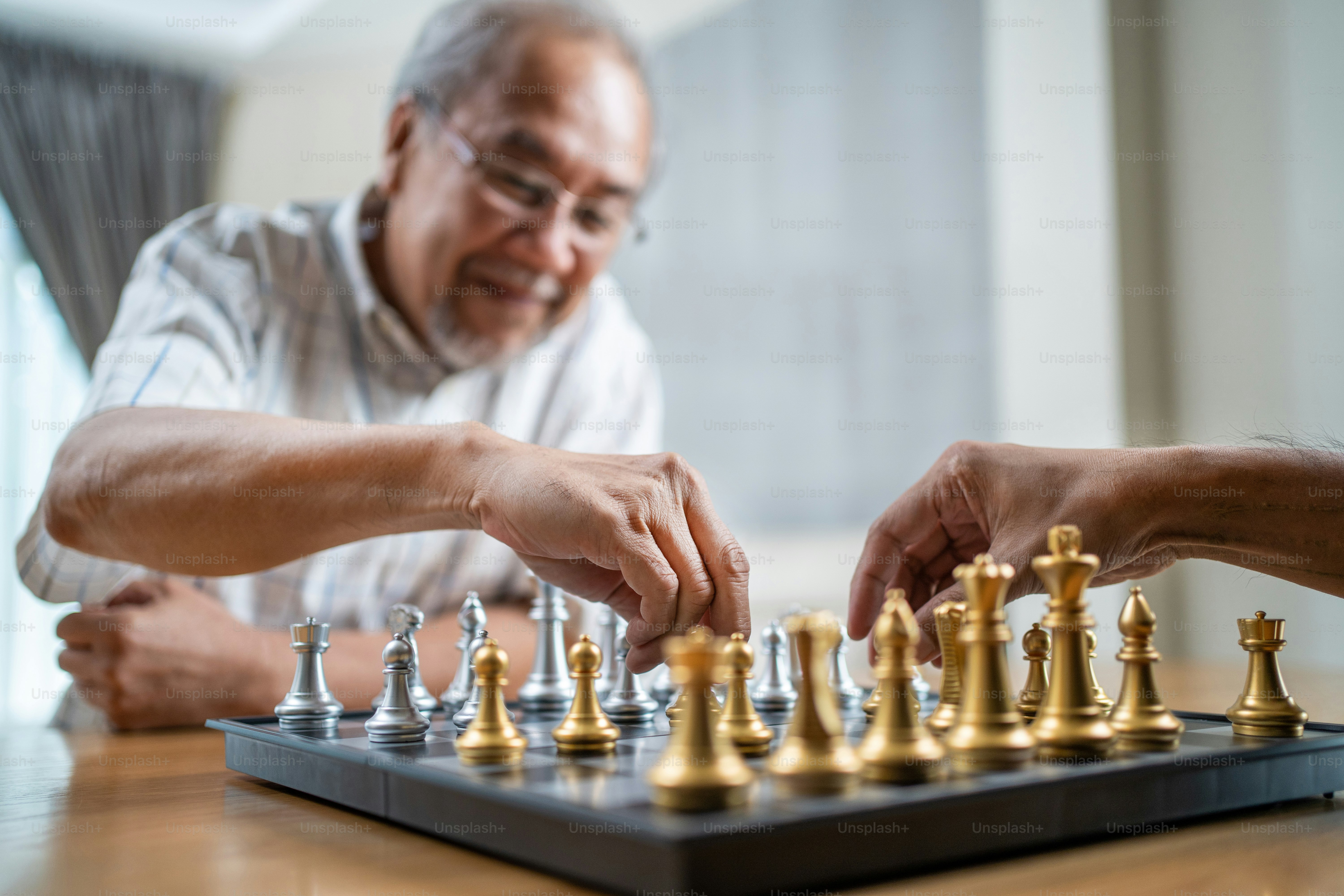 Asian Senior Old male spend leisure time, stay home after retirement. Happy smiling Elderly man enjoy activity in house playing chess game with friend together. Hospital Healthcare and medical concept