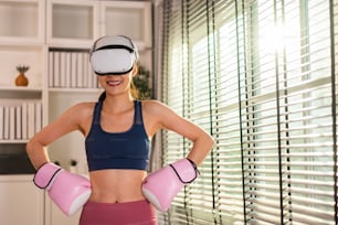 スポーツウーマンの肖像画は、革新的な技術VRメガネを使用して運動します。バーチャルリアリティヘッドセットを装着し、自宅でボクシングの戦いのトレーニングをしながらゲームコントローラーを保持する魅力的な美しい女の子。