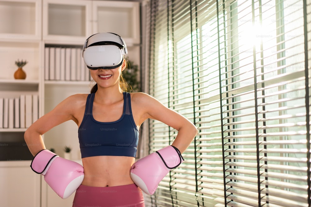 Il ritratto della sportiva usa gli occhiali VR di tecnologia innovativa per esercitarsi. Bella ragazza attraente che indossa cuffie per realtà virtuale e tiene il controller di gioco mentre fa allenamento di combattimento di boxe a casa.