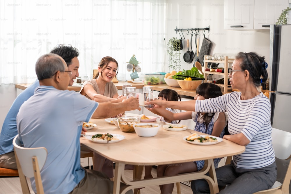 La grande famiglia felice asiatica pranza sul tavolo da pranzo insieme in casa. I nonni anziani, la giovane coppia e le figlie piccole si sentono felici, gustando il cibo in casa. Concetto di relazione di attività.