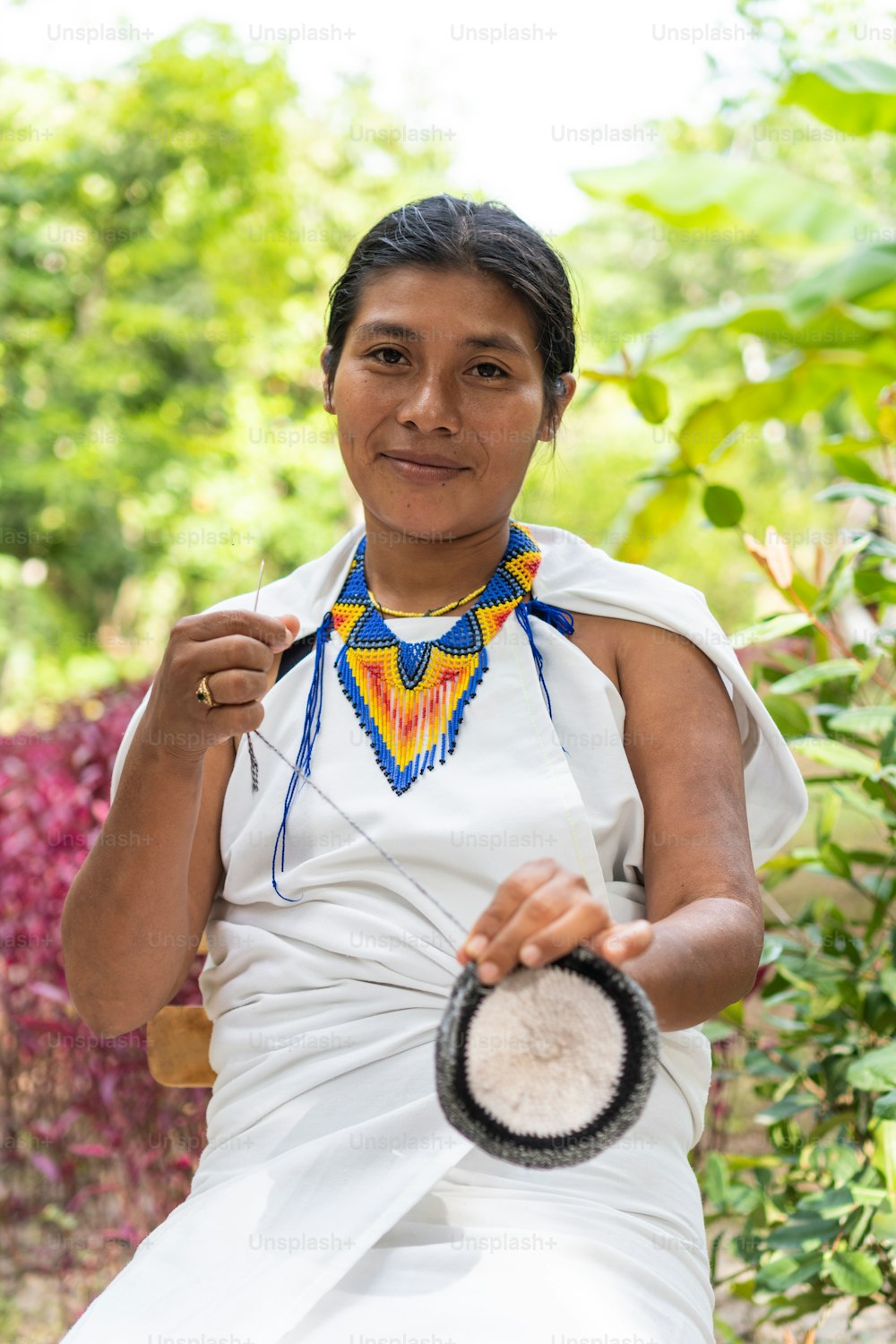 Indigene Frau aus der Sierra Nevada de Santa Marta in traditioneller Kleidung webt in die Kamera.