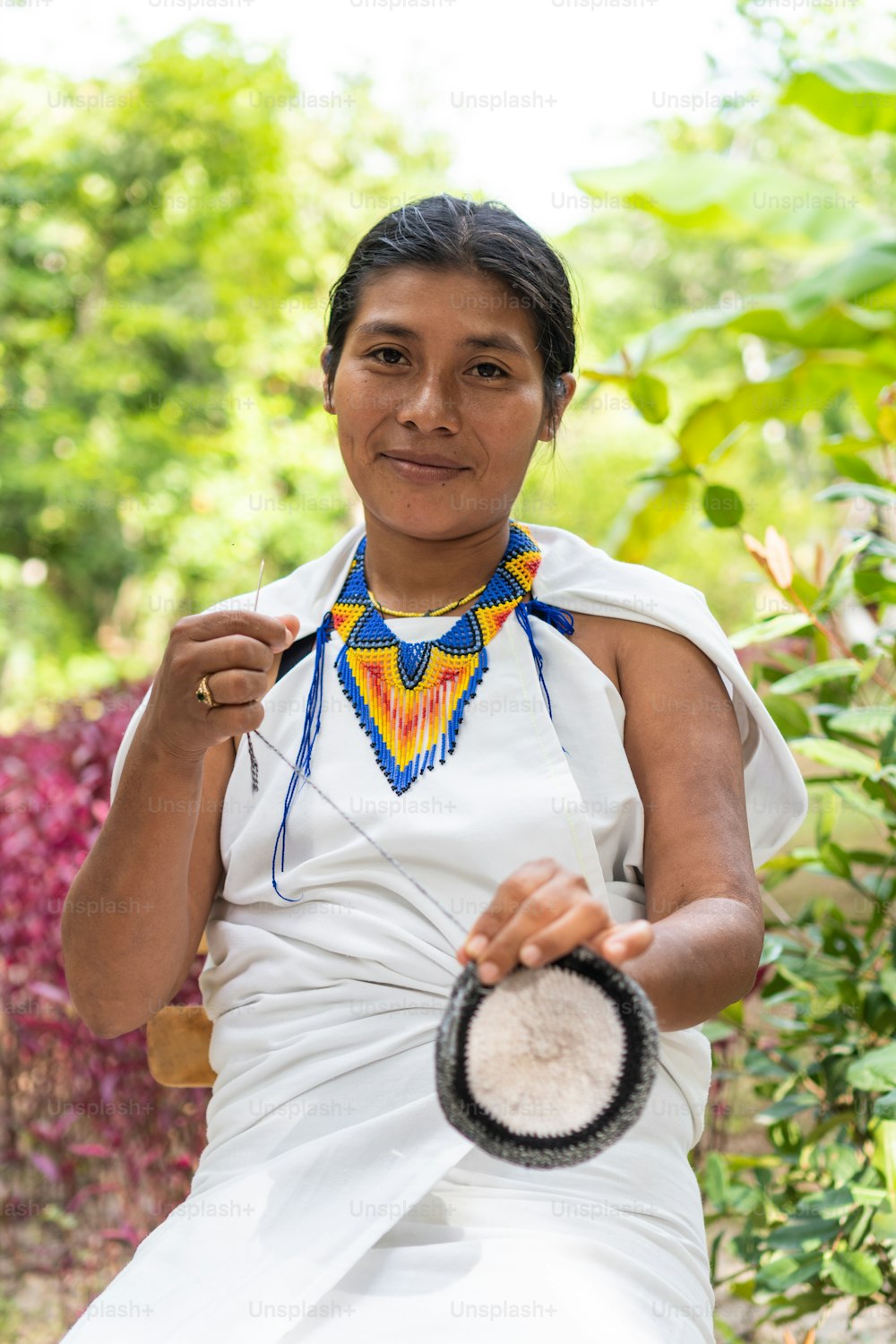 Indigenous woman from the Sierra Nevada de Santa Marta in traditional clothing weaving looking at the camera.