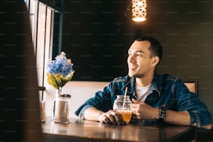 Fröhlicher und lächelnder junger lateinamerikanischer Mann, der an einem Restauranttisch ein Eisgetränk trinkt. Lifestyle-Konzept