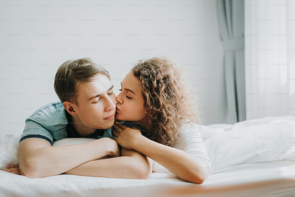 Young Happy Caucasian woman kissing her boyfriends on cheek while lying on the bed