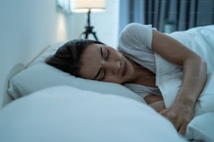 Bella donna asiatica sdraiata sul letto in camera da letto, sognando di notte. Attraente giovane femmina in pigiama che dorme da sola su un comodo cuscino e una coperta accogliente in una stanza buia per l'assistenza sanitaria a casa.