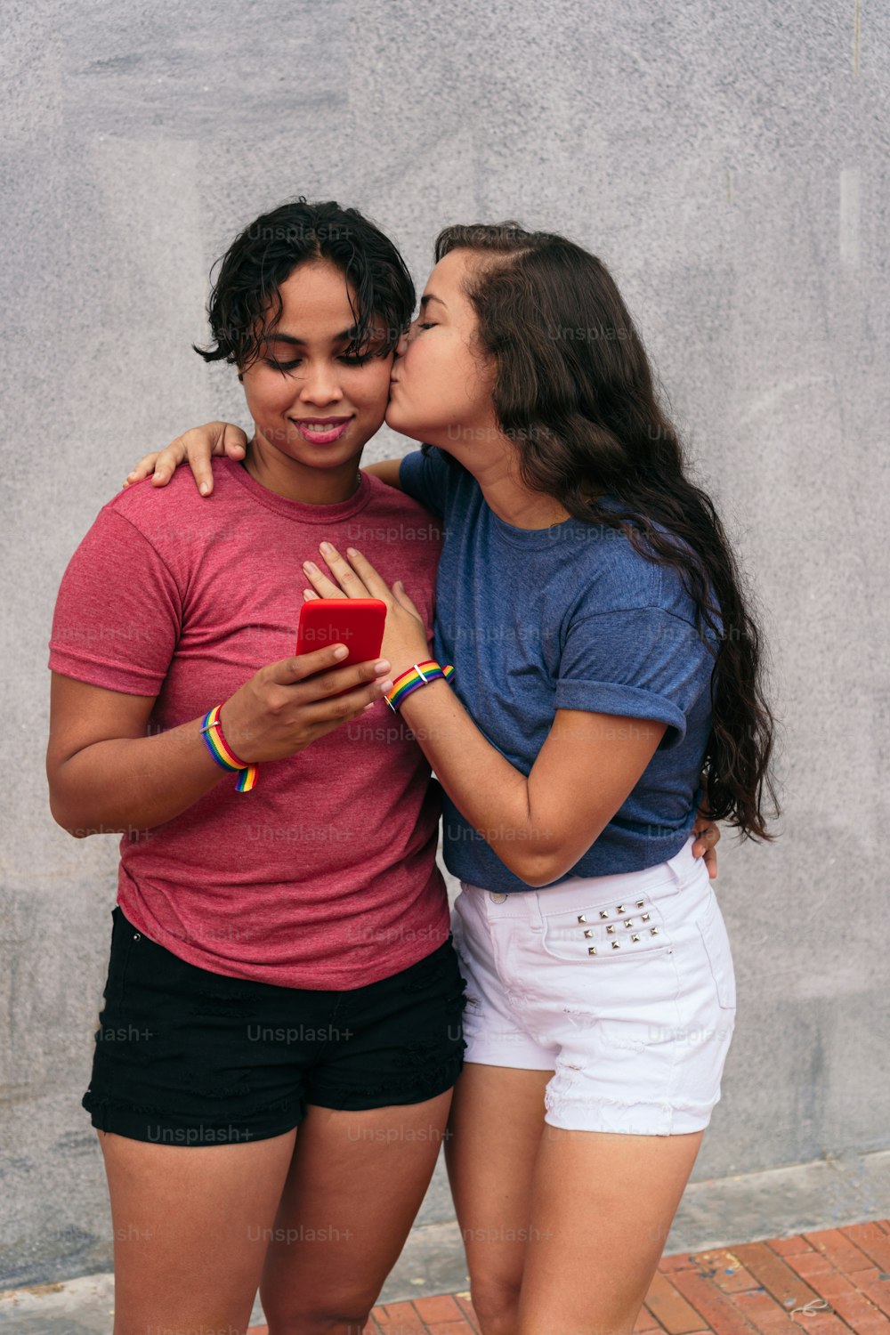 Latina couple takes selfie and smiles. Woman kissing her partner with a cell phone.
