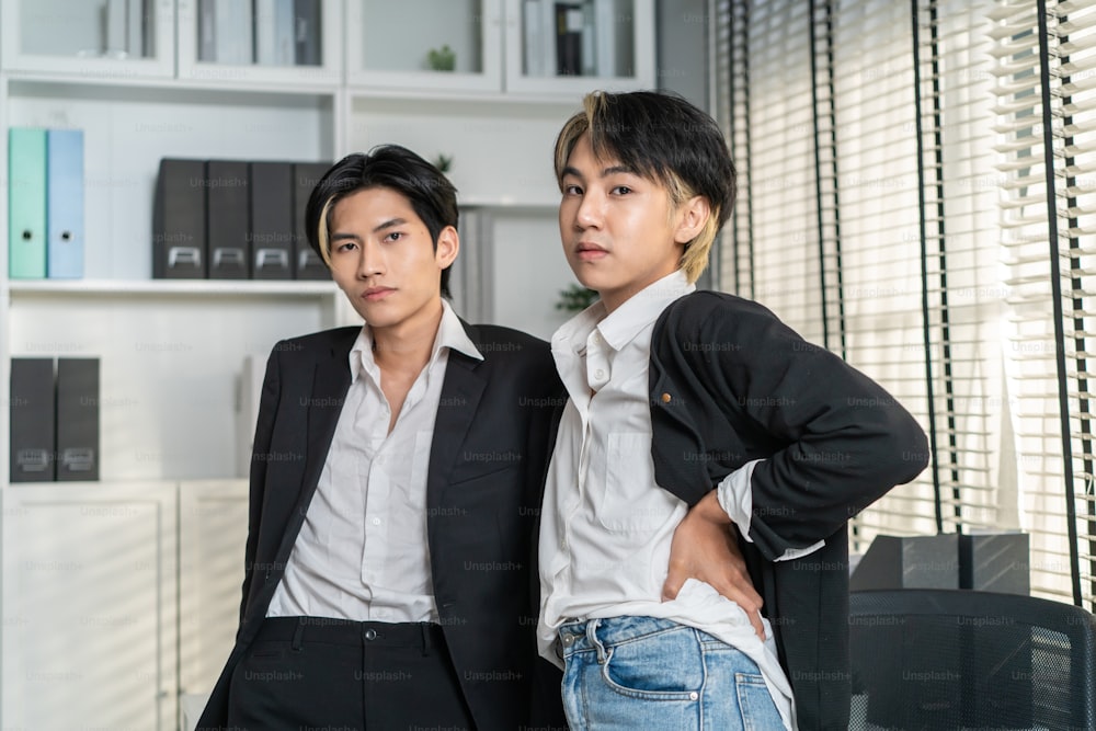 Portrait of Asian handsome businessman gay people working in office. Attractive male lgbtq collegues in formal wear standing with gay pride happiness and confidence at workplace then looking at camera