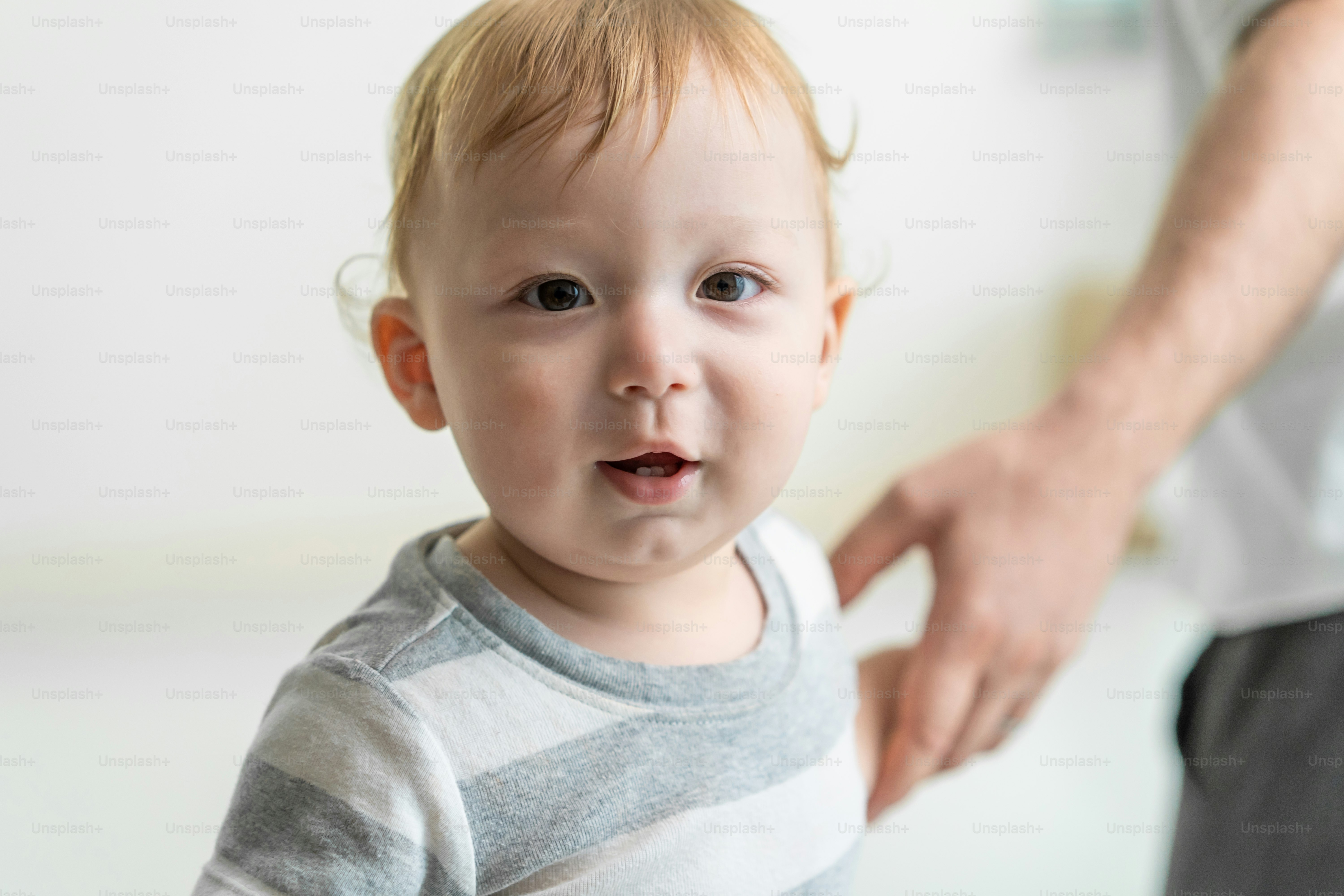 Portrait of Caucasian adorable baby boy kid smile, looking at camera. Cute little young toddler son feel happy while learn to walk on floor in house with parents support. Children development concept.
